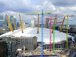 Construction site with cranes surrounding a stadium under development, cloudy sky above.