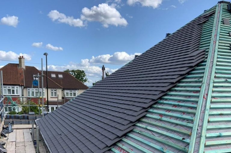 Slate roof tiles half Laid on a house roof with a cloudy blue sky in the background.