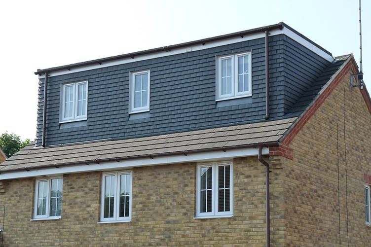 Modern three-storey house featuring a textured stone facade and a dark tiled roof as part of a attic conversion.