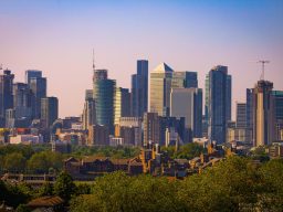 Skyline of a modern city with tall skyscrapers and green trees in the foreground.